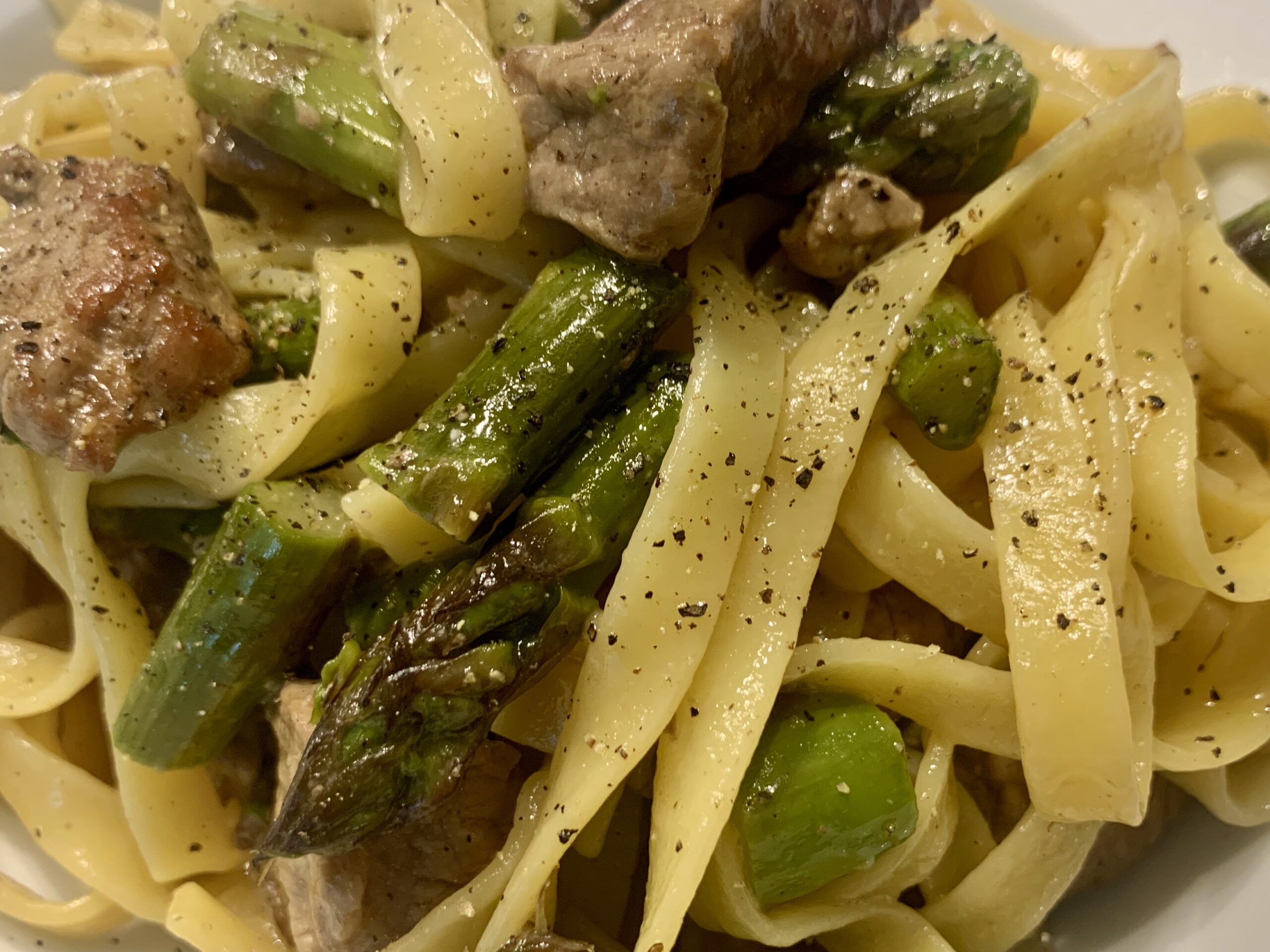 Fettuccine Alfredo mit grünem Spargel und Rinderfilet-Streifen auf einem Teller angerichtet.