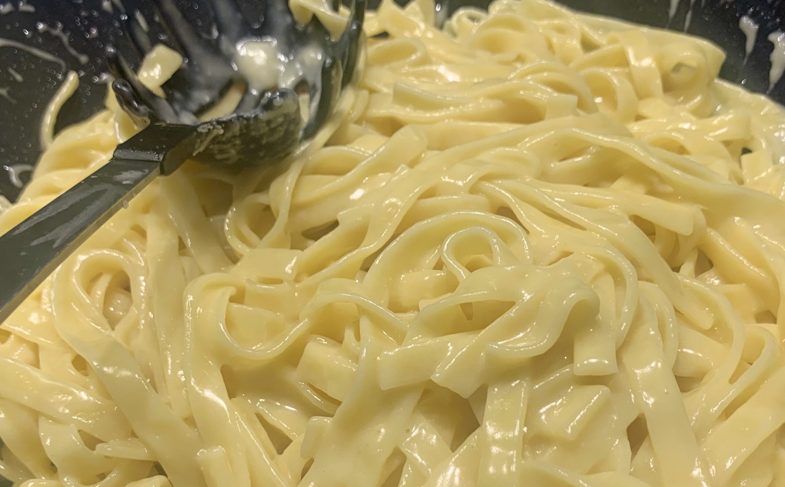 Fettuccine Alfredo glänzen in einer Wok-Pfanne.